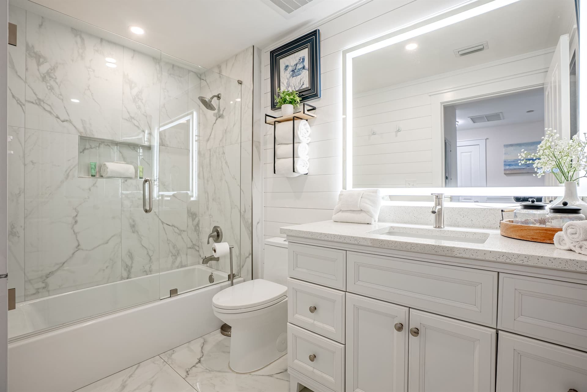 Bathroom with marble tile shower-tub combo and backlit vanity mirror
